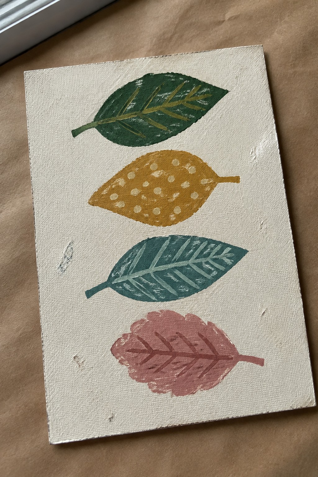 Four stylized leaves painted in green, gold, teal, and pink on white canvas.