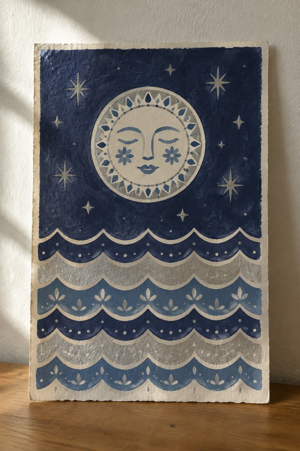 Moon face with flowers above layered blue waves and silver stars