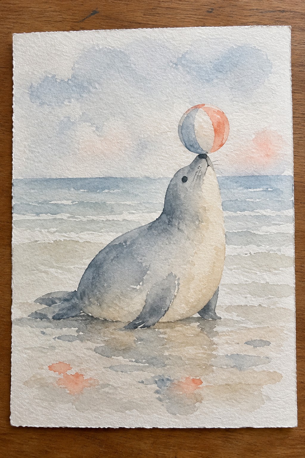 Watercolor seal balancing a colorful beach ball on its nose by the ocean.