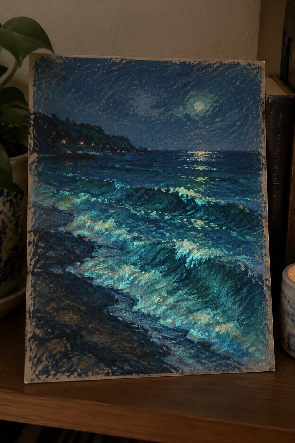 Impressionistic painting of moonlit blue waves crashing near dark shore on wooden table