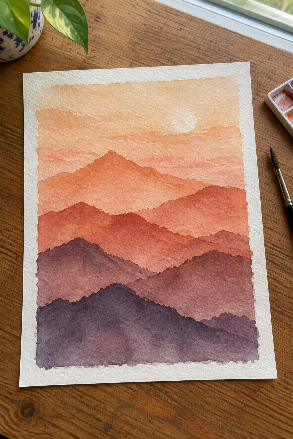 Watercolor painting of layered mountains in warm orange to purple tones with a white sun circle in a pale sky on white paper.