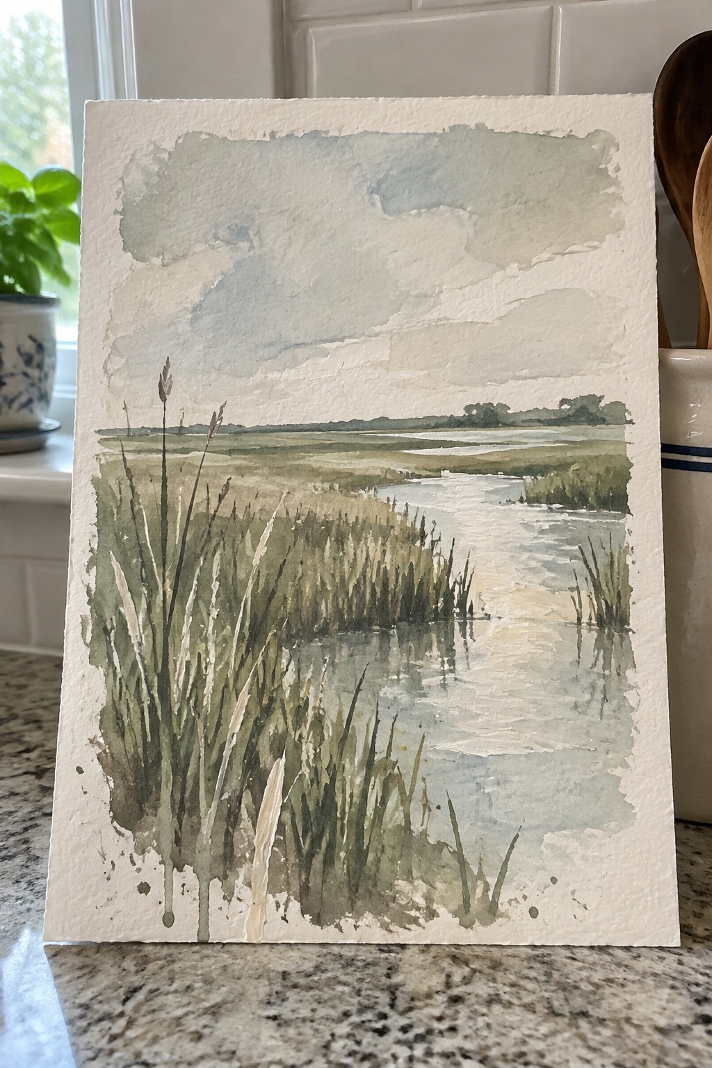 Watercolor marsh scene with tall reeds, winding creek, and cloudy sky on paper.