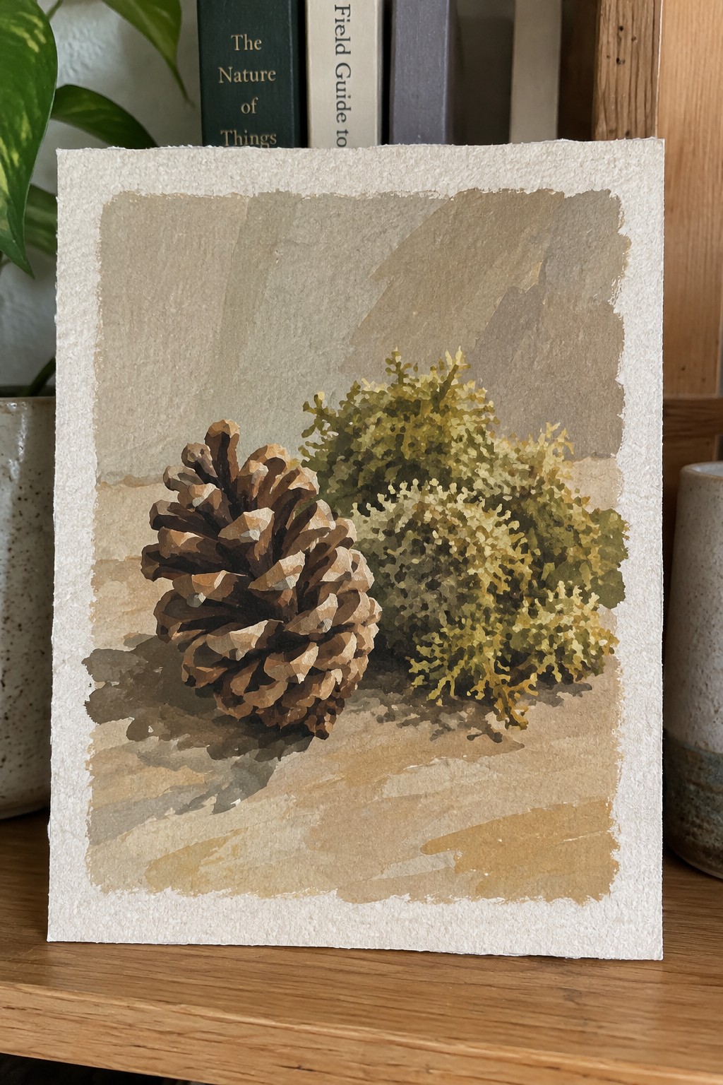 Watercolor painting of brown pinecone beside yellow-green bush on textured paper
