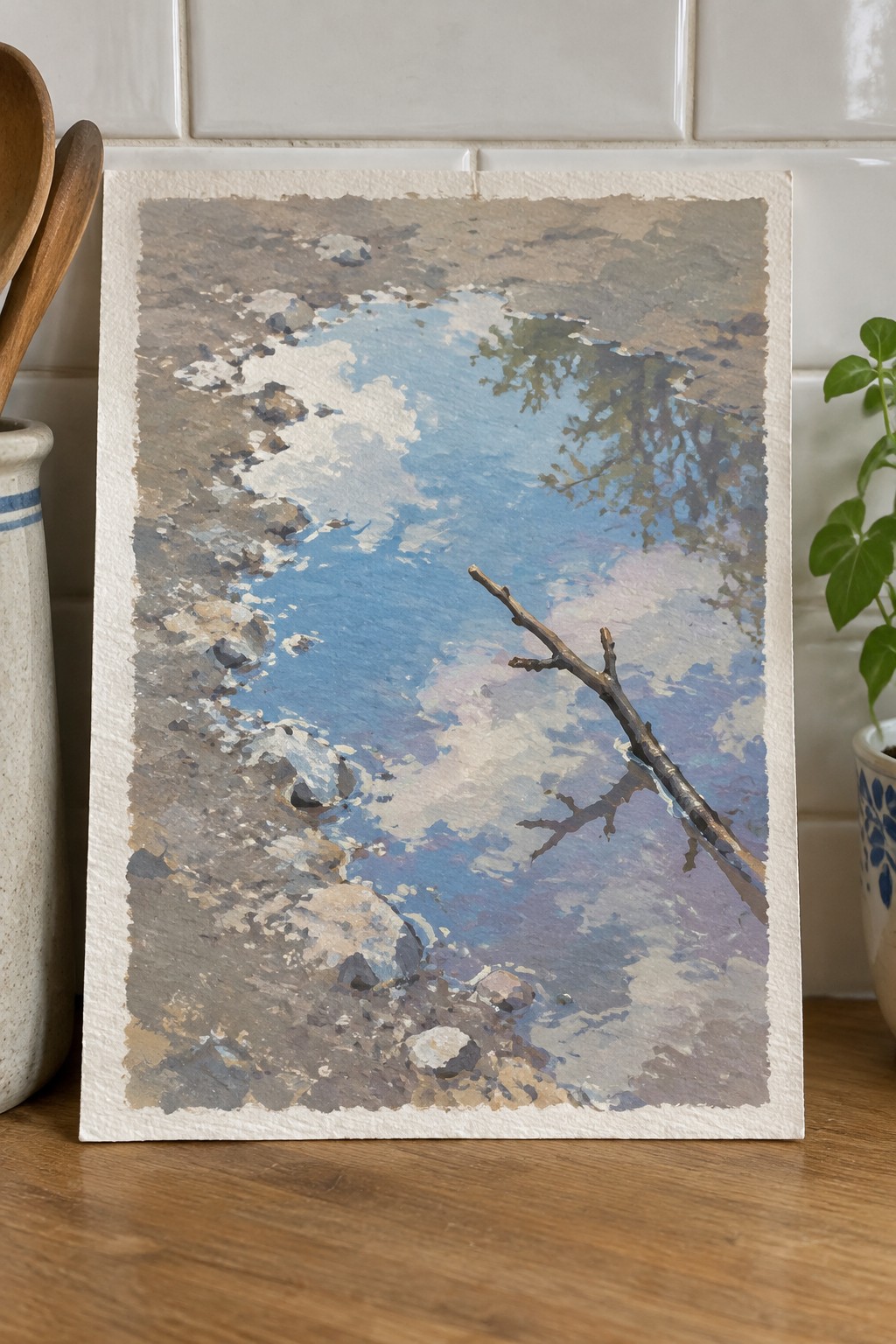 Watercolor painting of blue sky with clouds and bare branch on wooden table