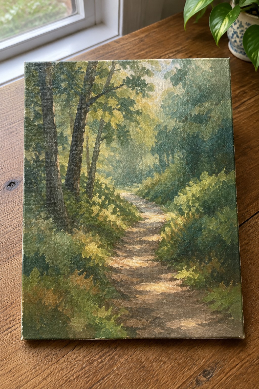 Oil painting of sunlit dirt path winding through dense green forest trees.
