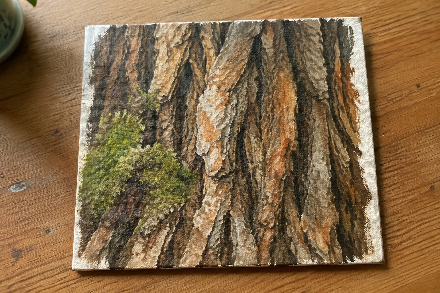 Painting of textured tree bark in browns with green moss on wooden table