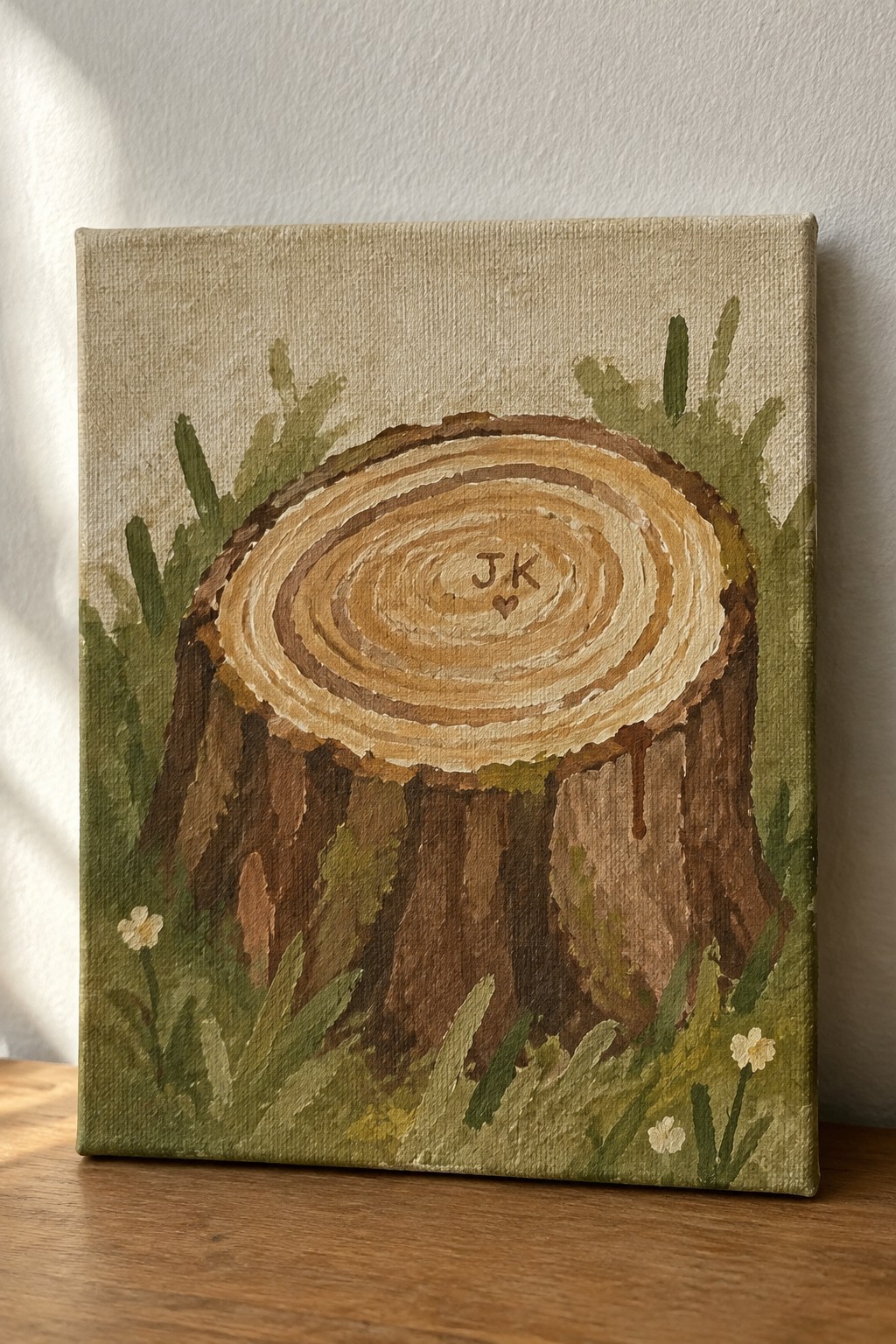 Canvas painting of tree stump cross-section with JK initials amid green foliage and flowers
