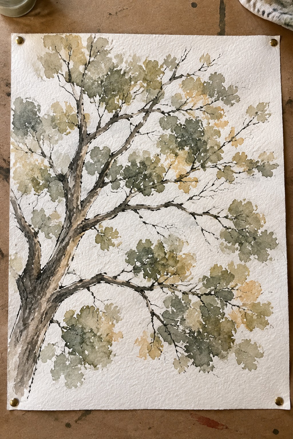 Watercolor painting of leafy tree in green and yellow tones pinned to wood surface