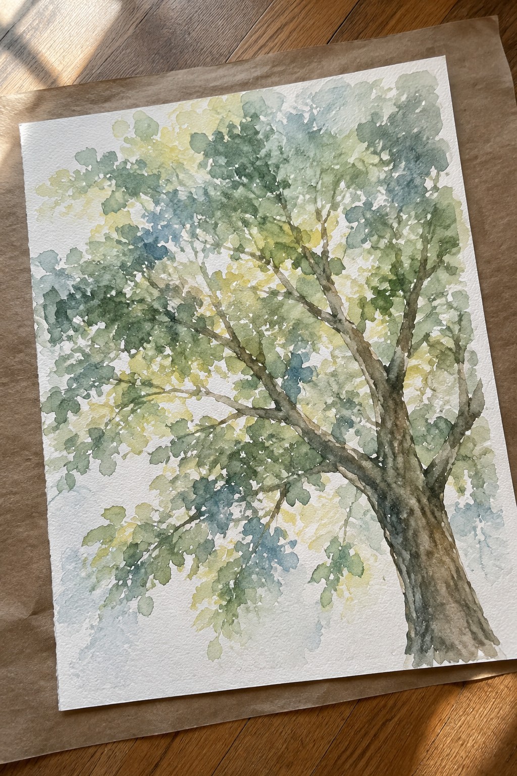 Watercolor painting of tree with green yellow leaves on white paper over wooden floor