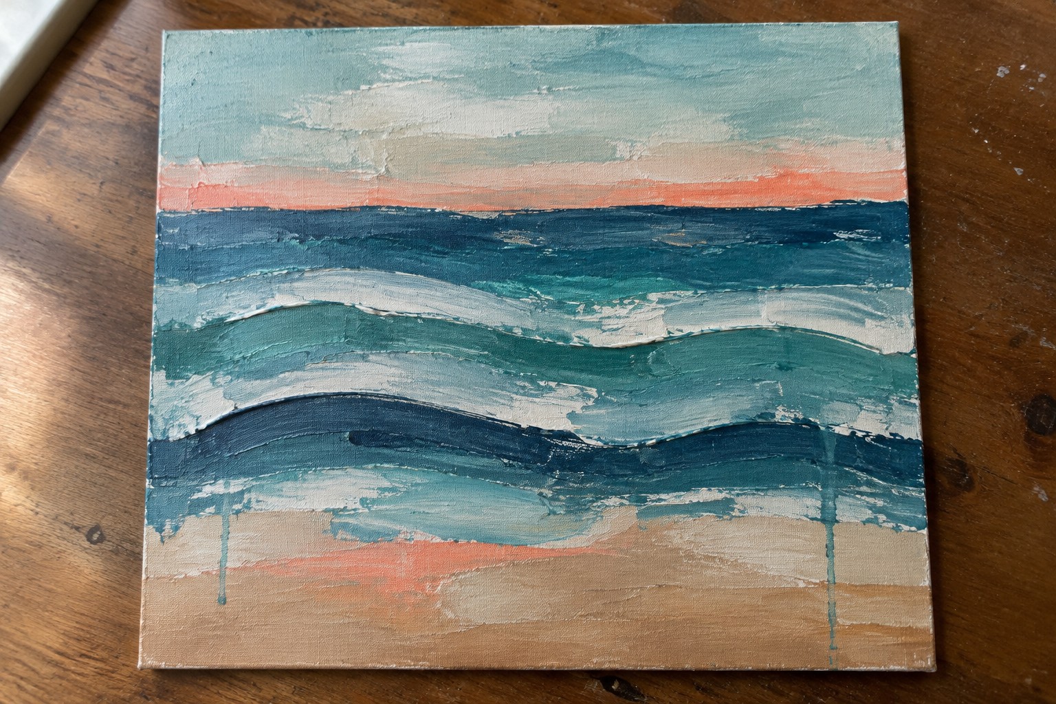 Abstract seascape painting with textured blue waves and sandy shore on wood table