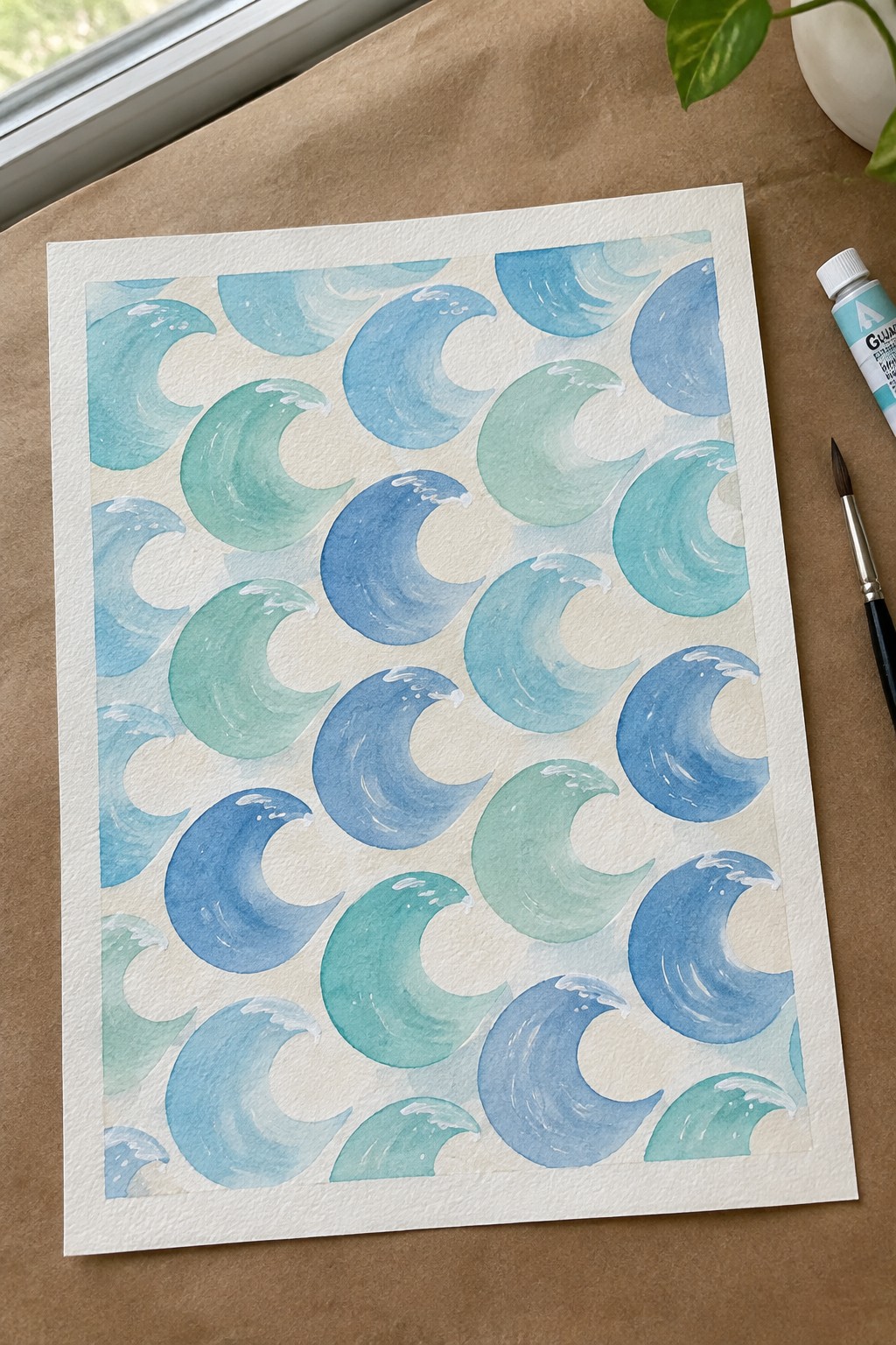 Watercolor painting of blue and green waves on white paper beside paint tube and brush