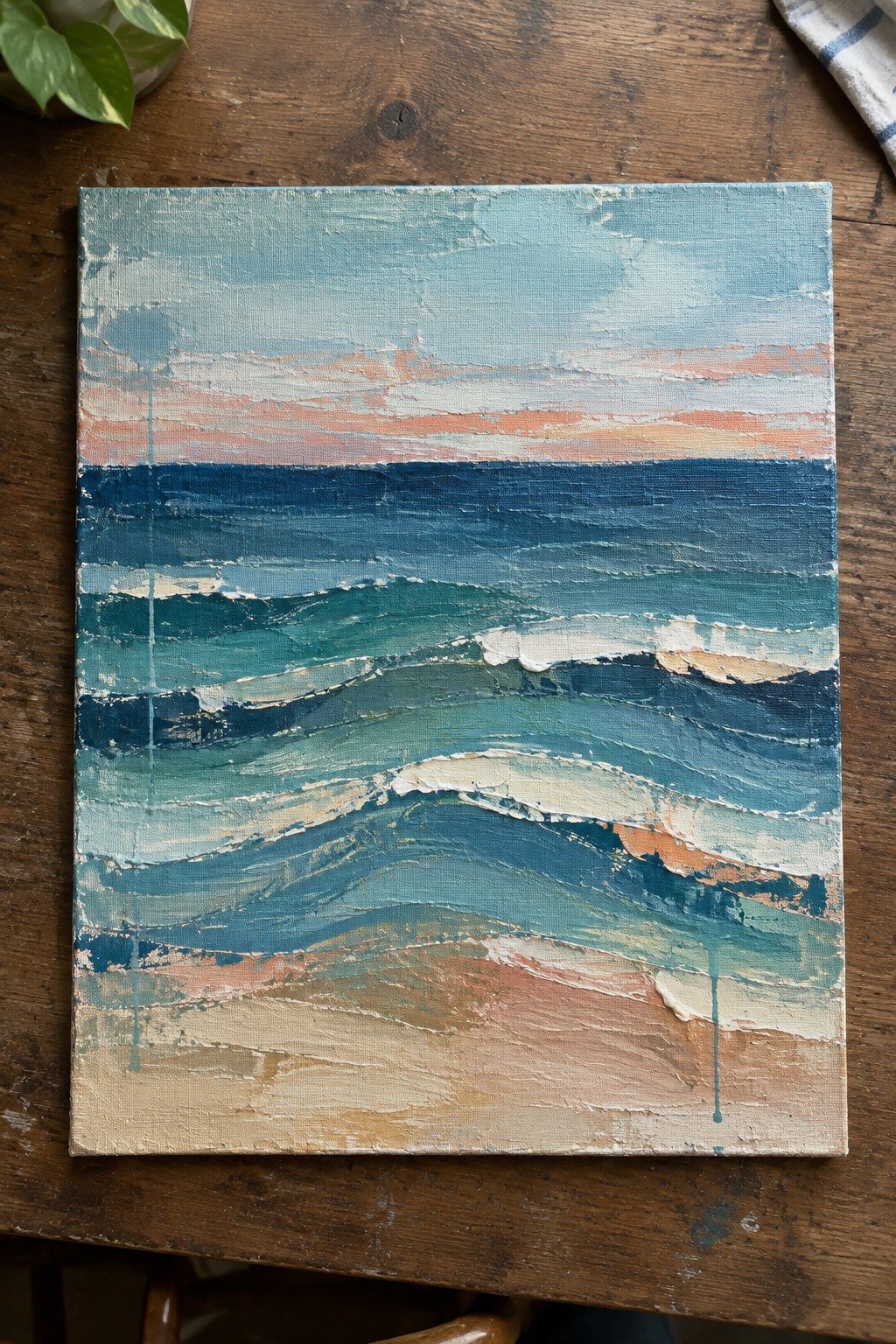 Abstract seascape painting with textured blue waves and sandy shore on wood table