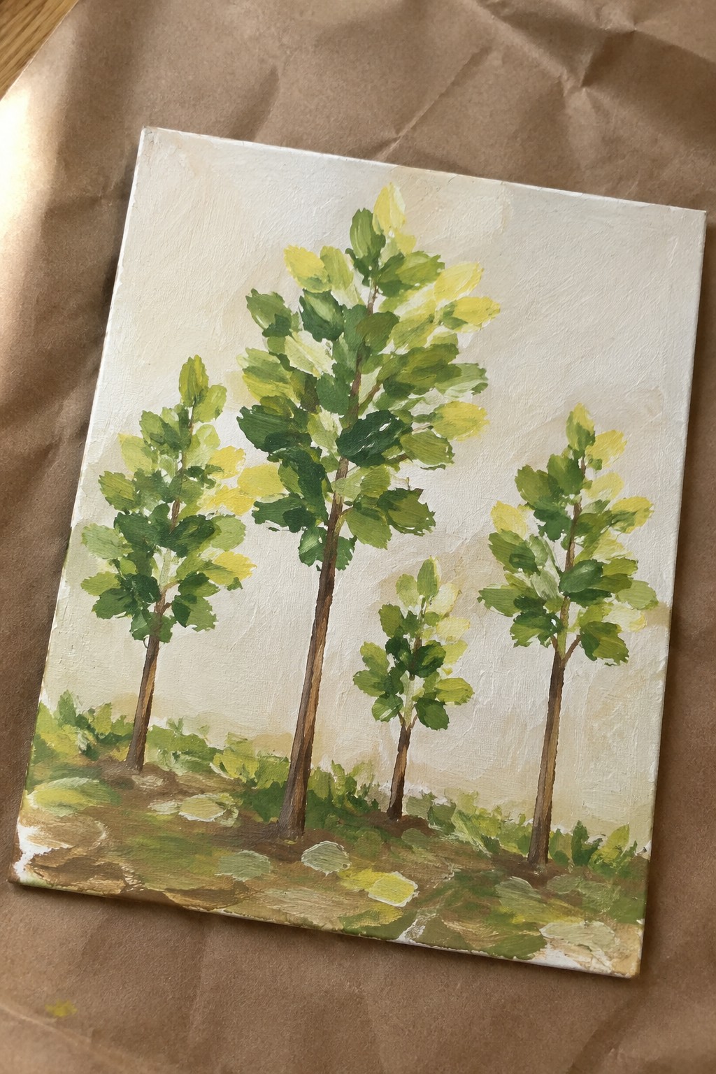Painting of trees with green-yellow leaves on canvas atop brown paper.
