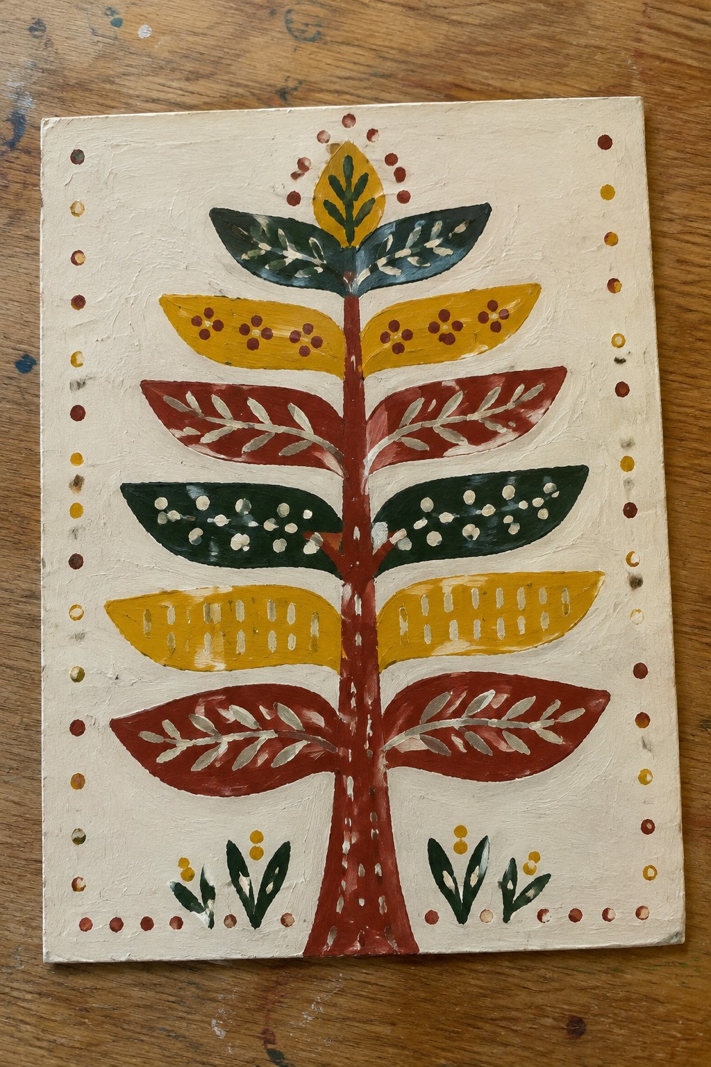 Stylized folk art tree with red trunk, patterned yellow-green leaves, and dotted border.