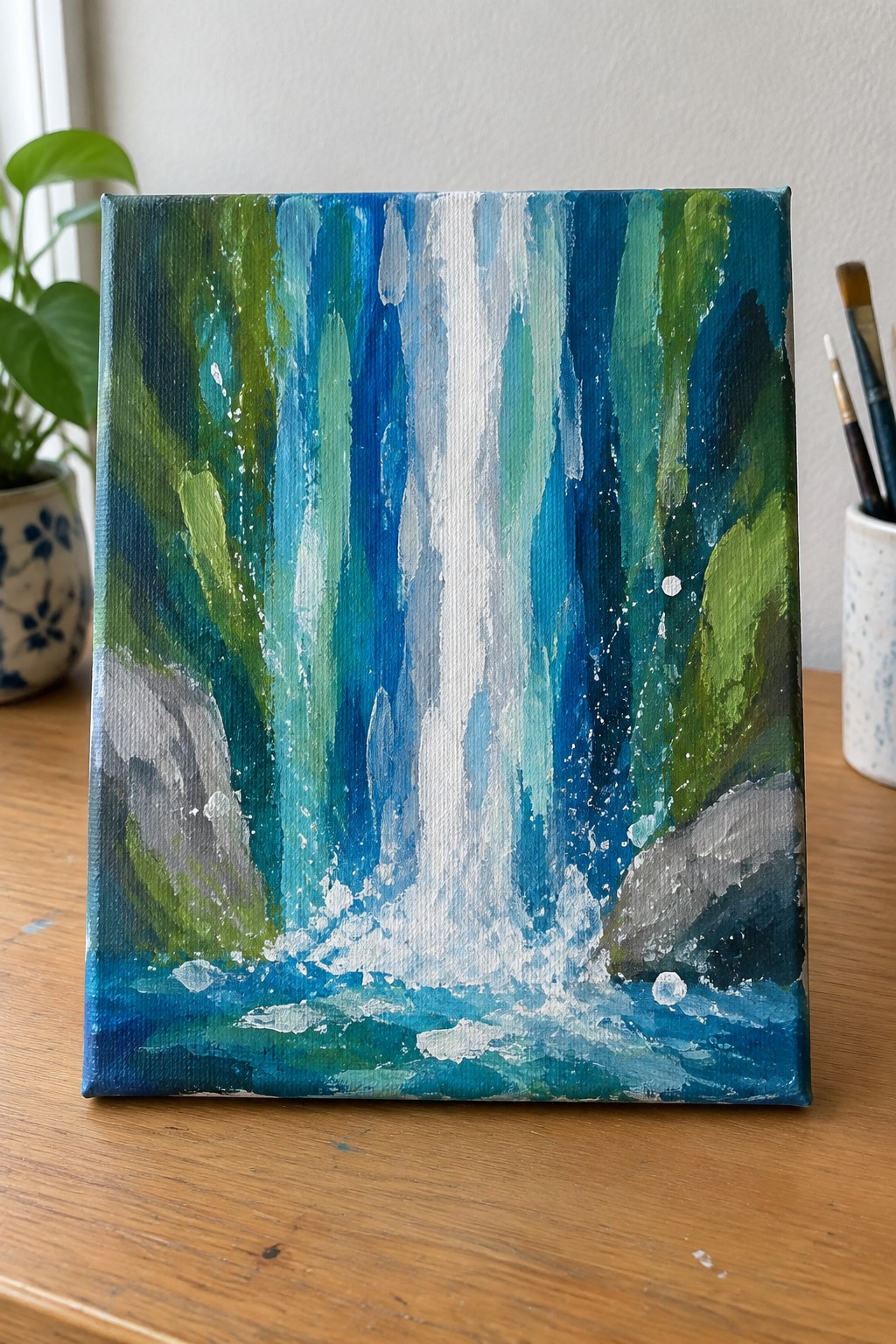 Square canvas with an abstract waterfall painted in vertical blue and green streaks, white water in the center, and a blue pool with gray rocks at the bottom.