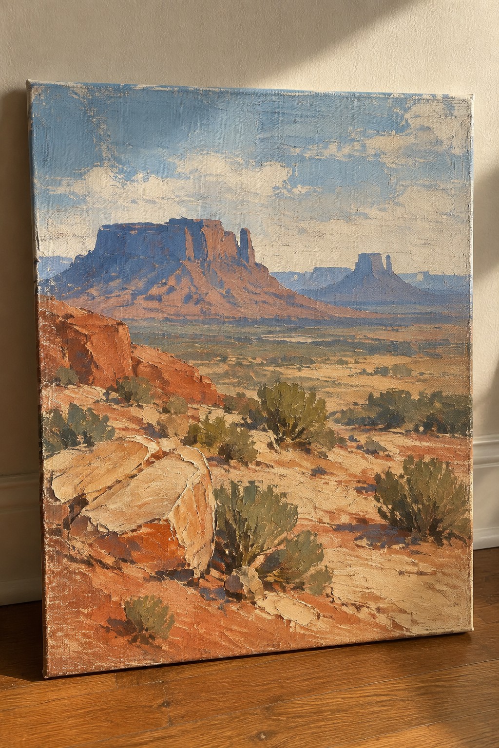 Oil painting of red rock mesas with rocky desert foreground and blue cloudy sky.