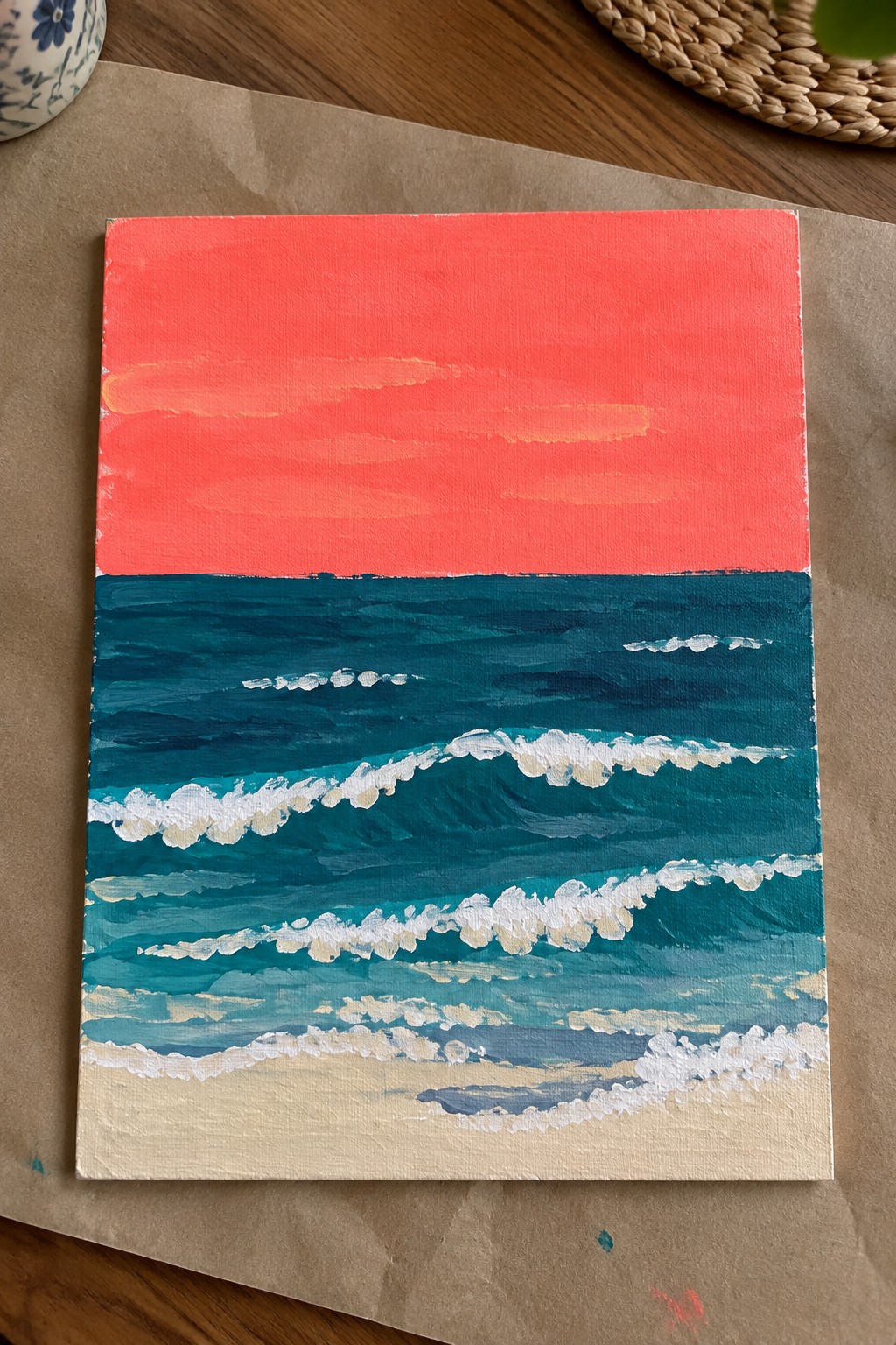Acrylic painting of red sky over teal waves with white foam on sandy beach