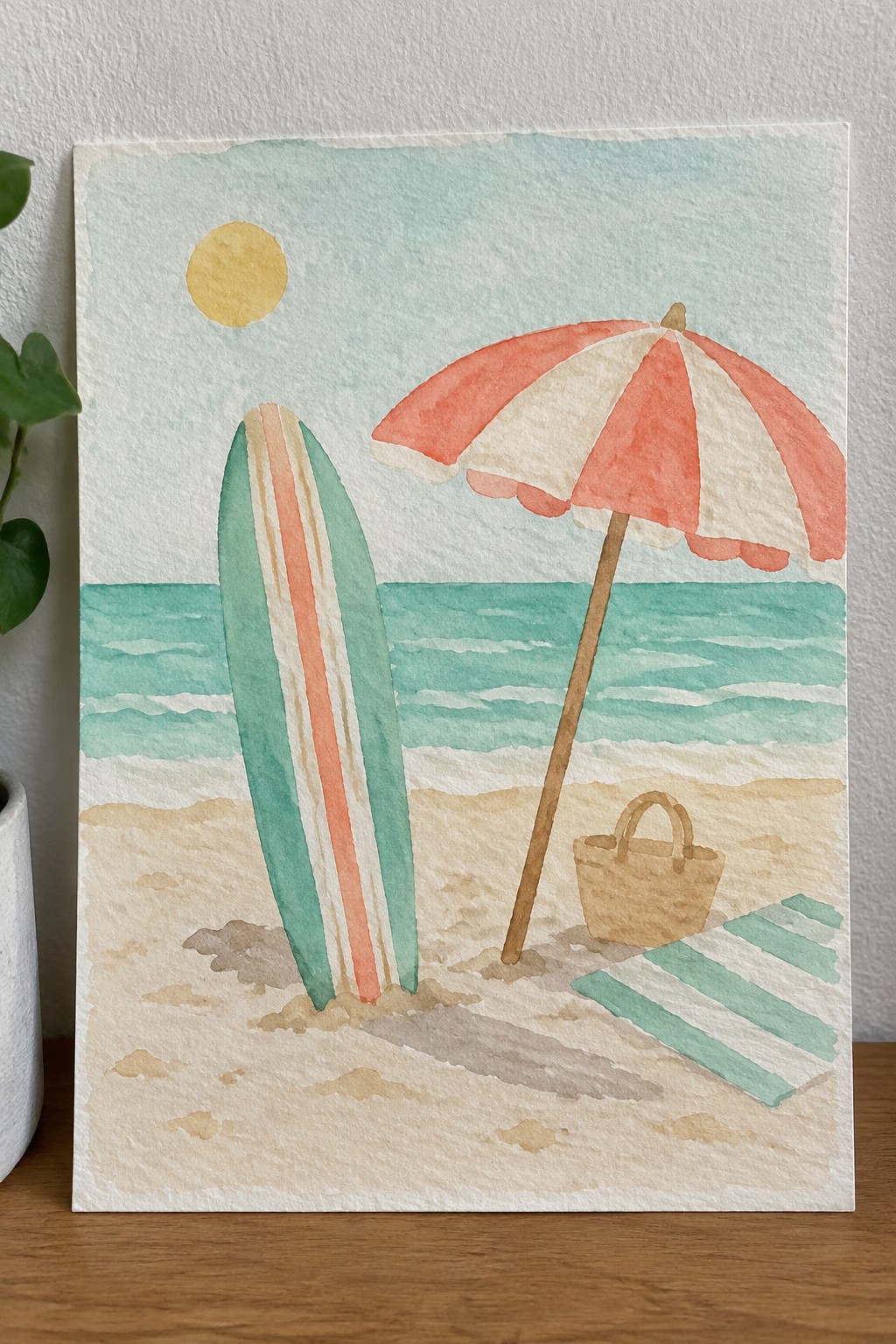 A watercolor beach scene showing a surfboard in the sand, a red and white umbrella, a basket, and a striped towel beside turquoise waves with a yellow sun overhead.