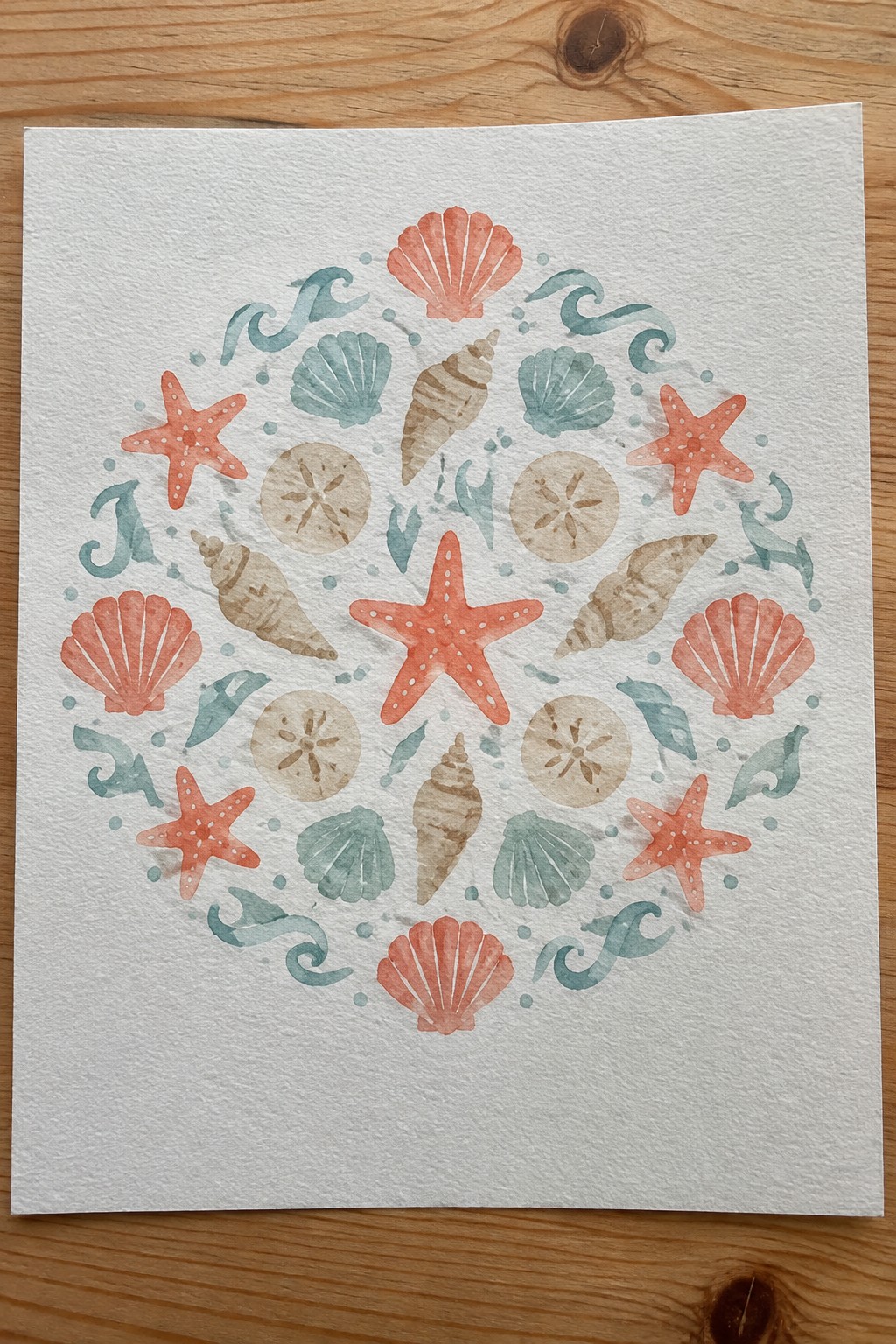 Watercolor mandala of coral starfish, seashells, sand dollars, and teal waves in a circle.