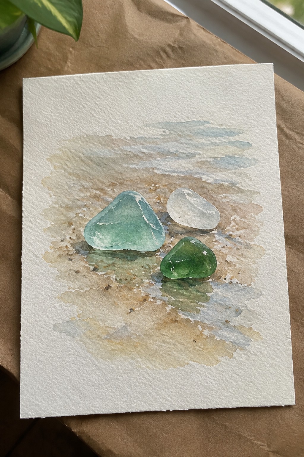 Three sea glass stones in turquoise, white, and green on watery sand wash