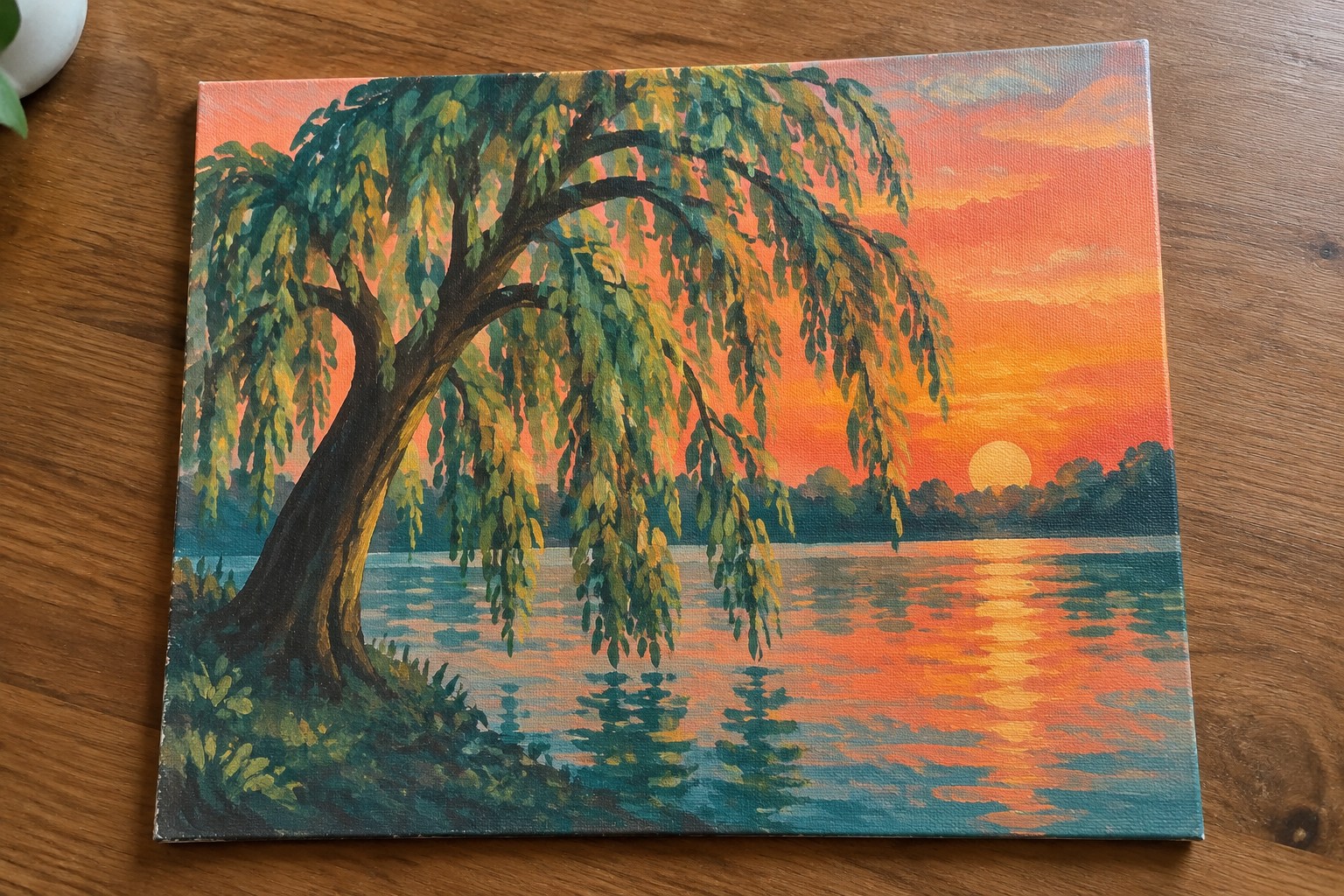 Weeping willow tree by a lake reflecting vibrant orange sunset sky and hills