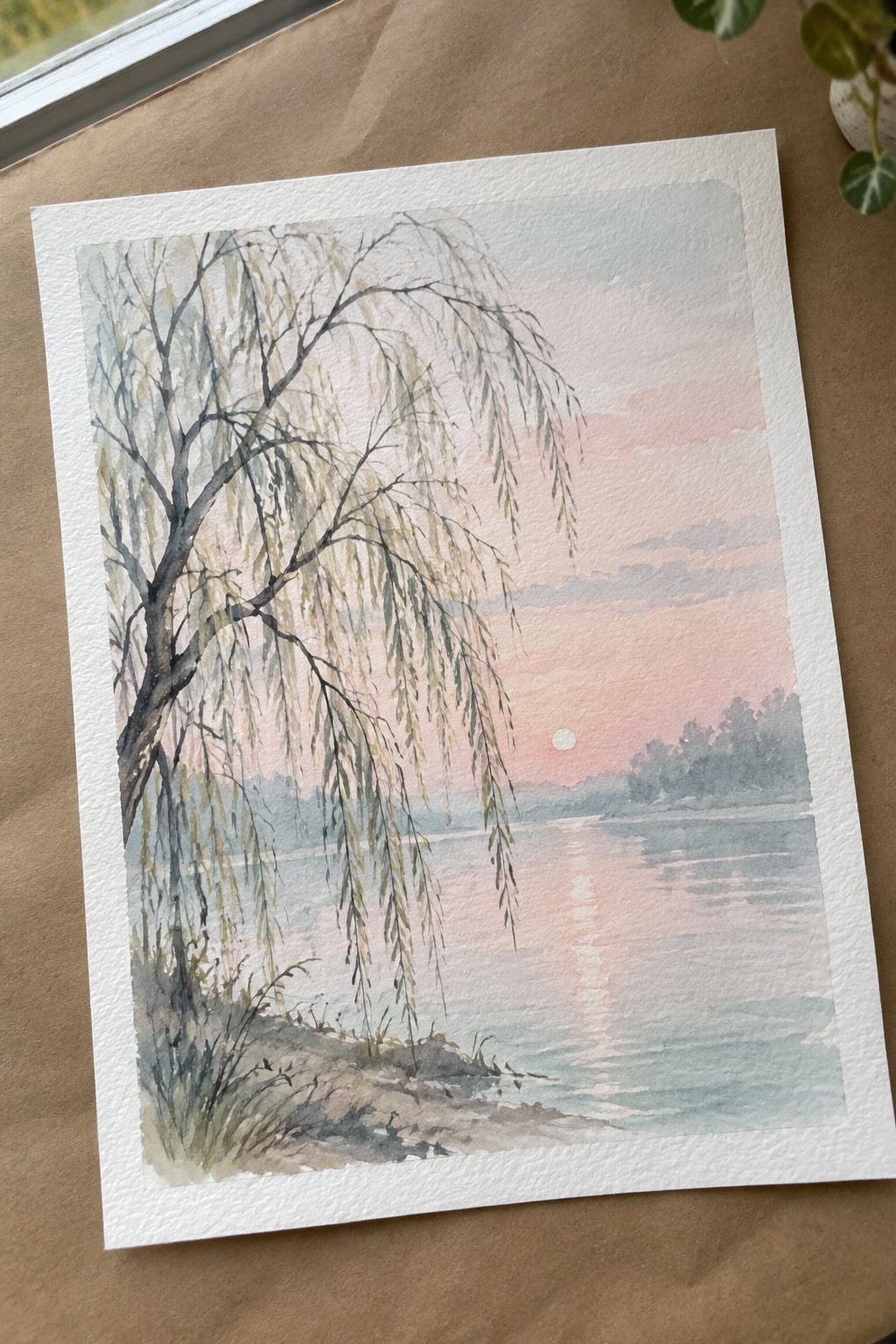 Watercolor of weeping willow tree by calm lake under pink sunset sky with sun reflection.