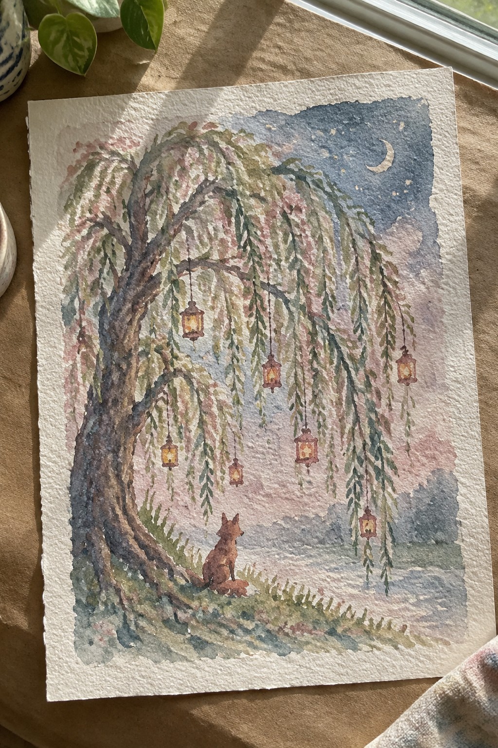 Watercolor of fox beneath lantern-hung weeping willow under starry night sky.