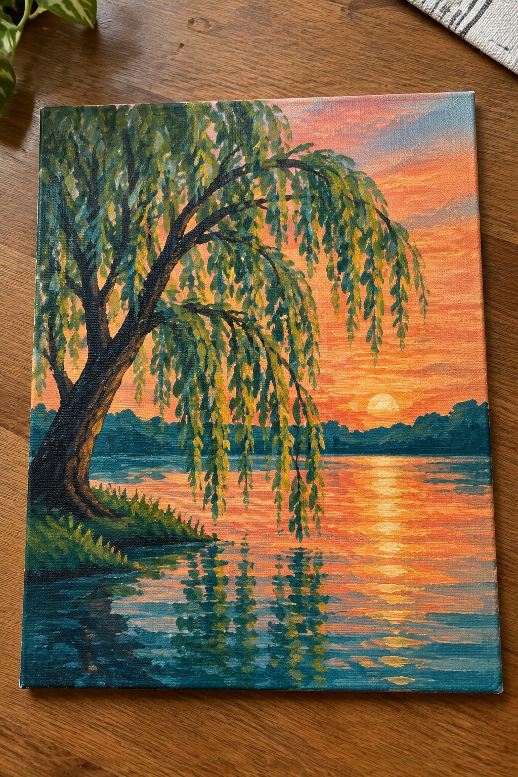 Weeping willow tree by a lake reflecting vibrant orange sunset sky and hills