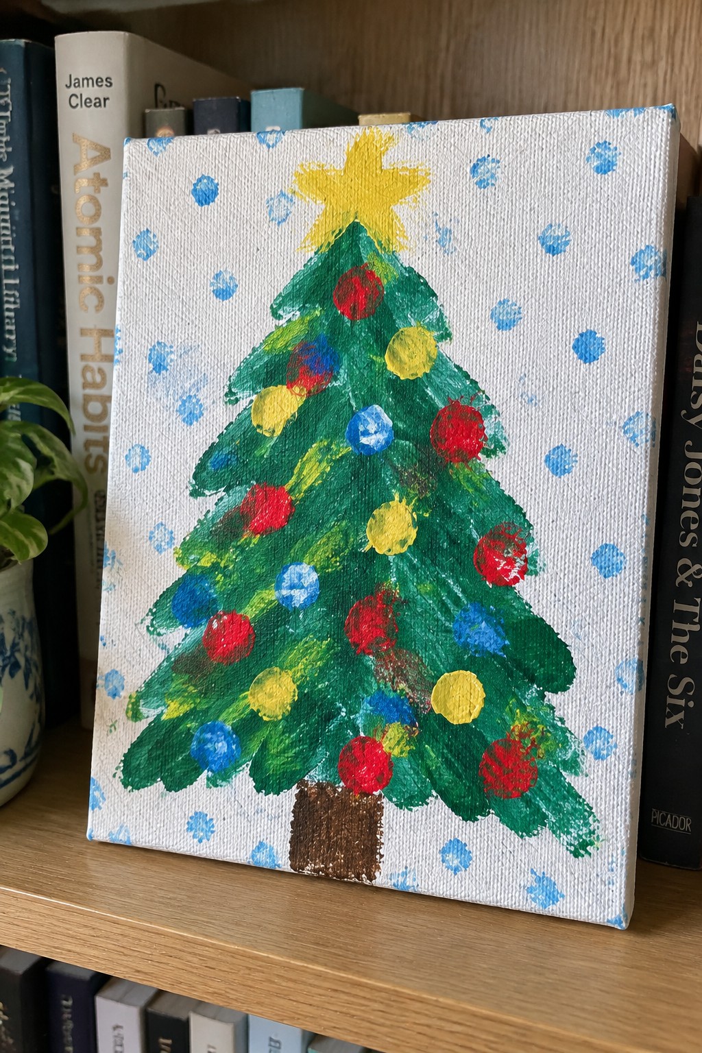 Colorful Christmas tree painting on canvas amid books on wooden shelf