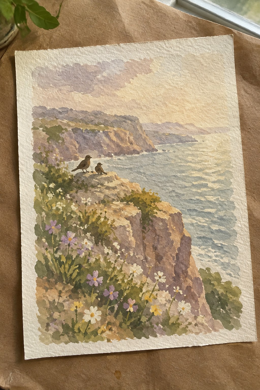 Watercolor of two birds on a rocky cliff overlooking the sea amid wildflowers