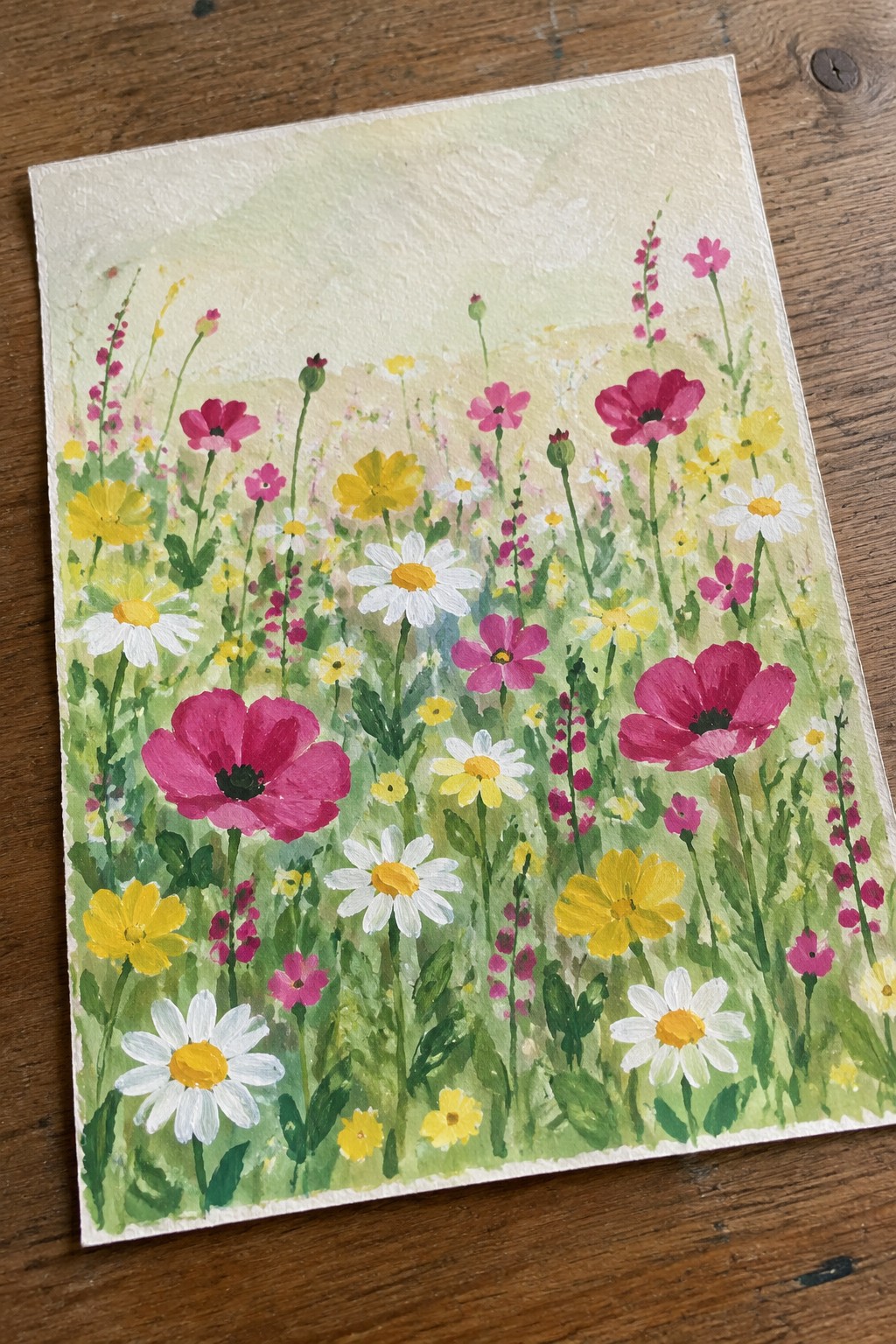 Vibrant watercolor meadow with pink poppies, white daisies, and yellow wildflowers on wood