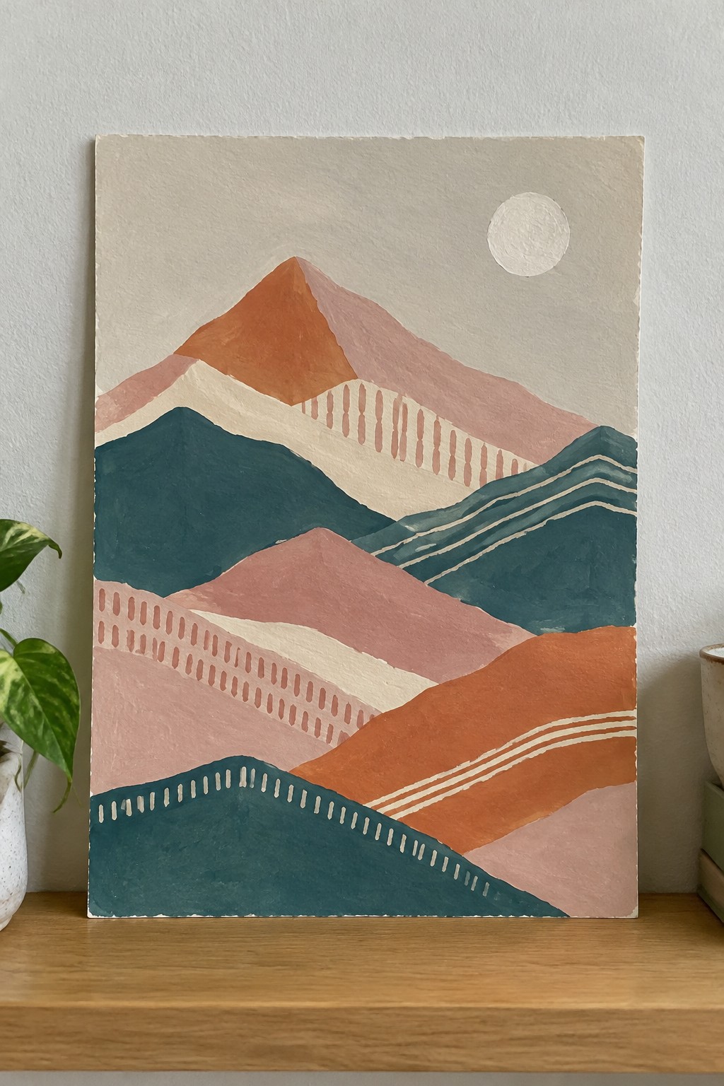 Abstract mountain painting in orange pink teal with dotted lines and sun on wooden shelf