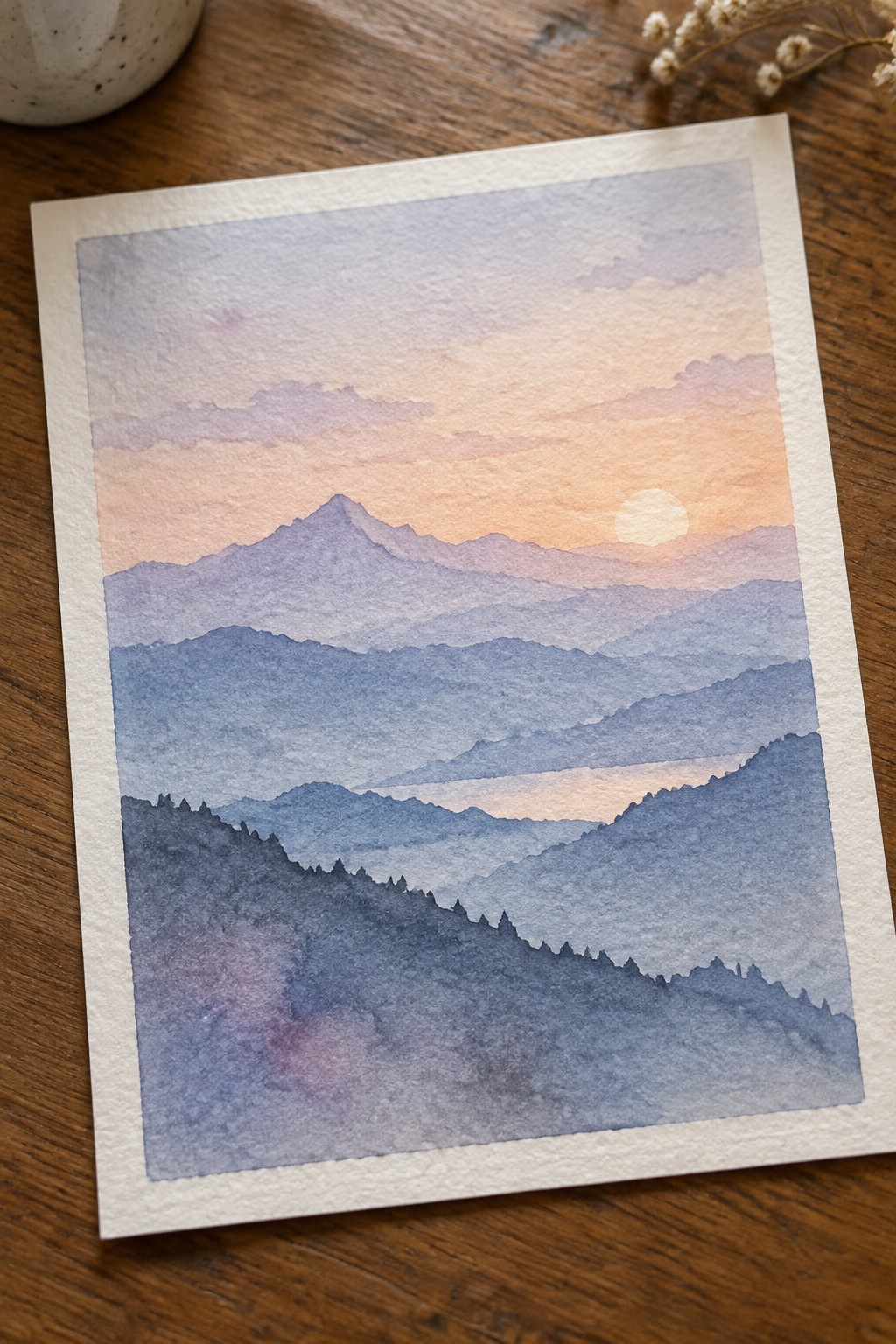 Layered blue mountains beneath a soft orange-pink sunset sky with glowing sun.
