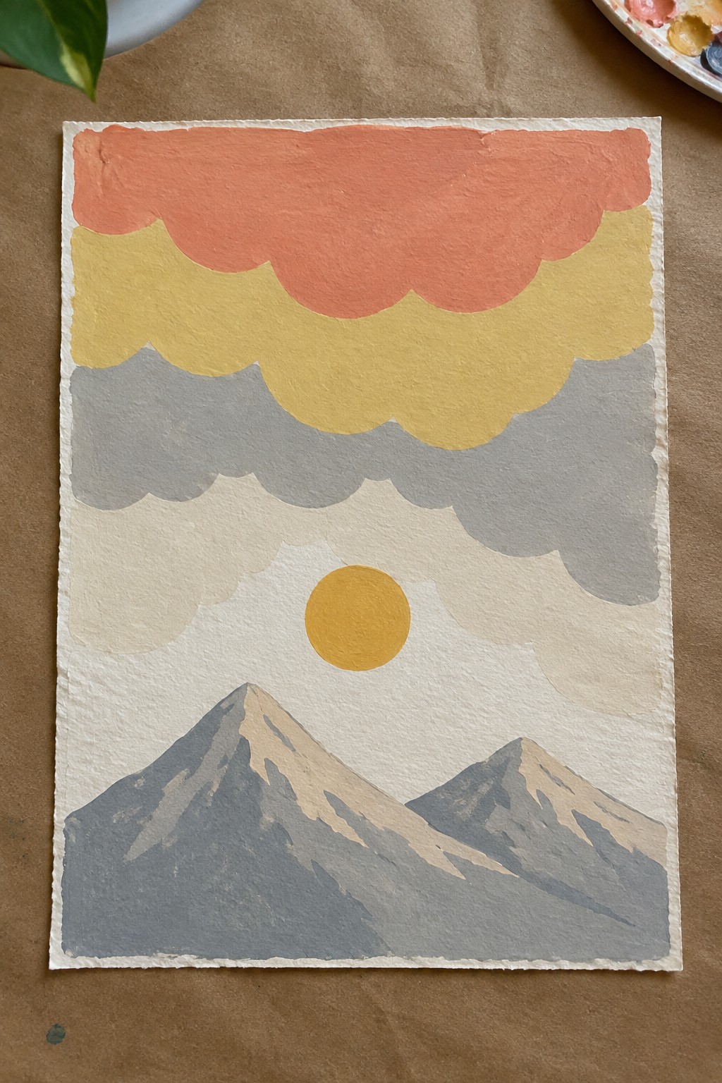 Layered scalloped clouds in orange, yellow, and gray over mountains with yellow sun.