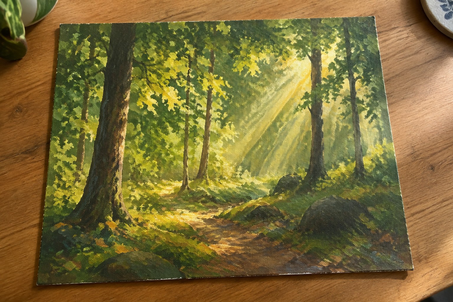 Sunlit forest path winding among tall green trees with golden light rays on wood table