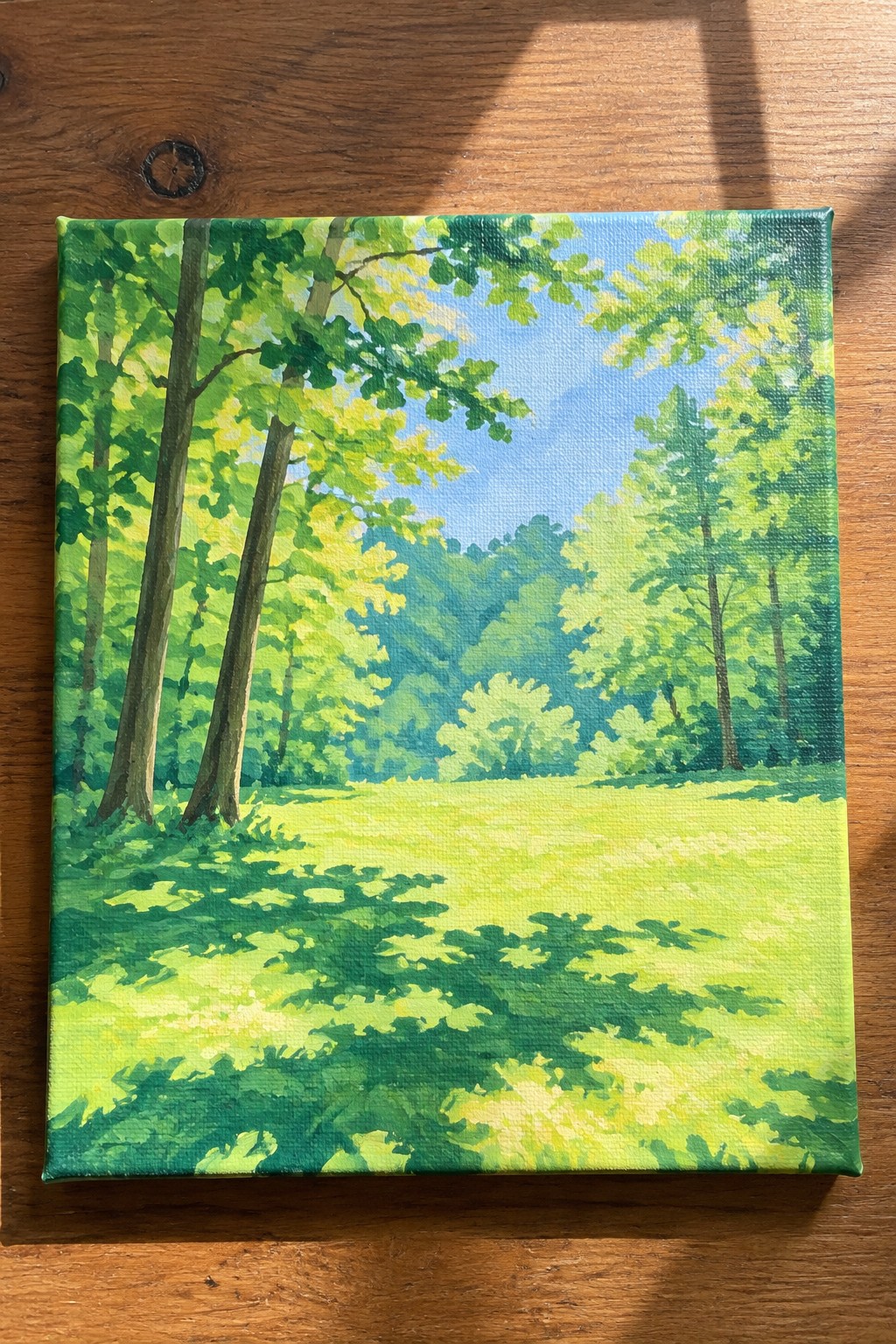 A painting of a sunny forest clearing with tall trees casting green shadows across a bright grassy field.