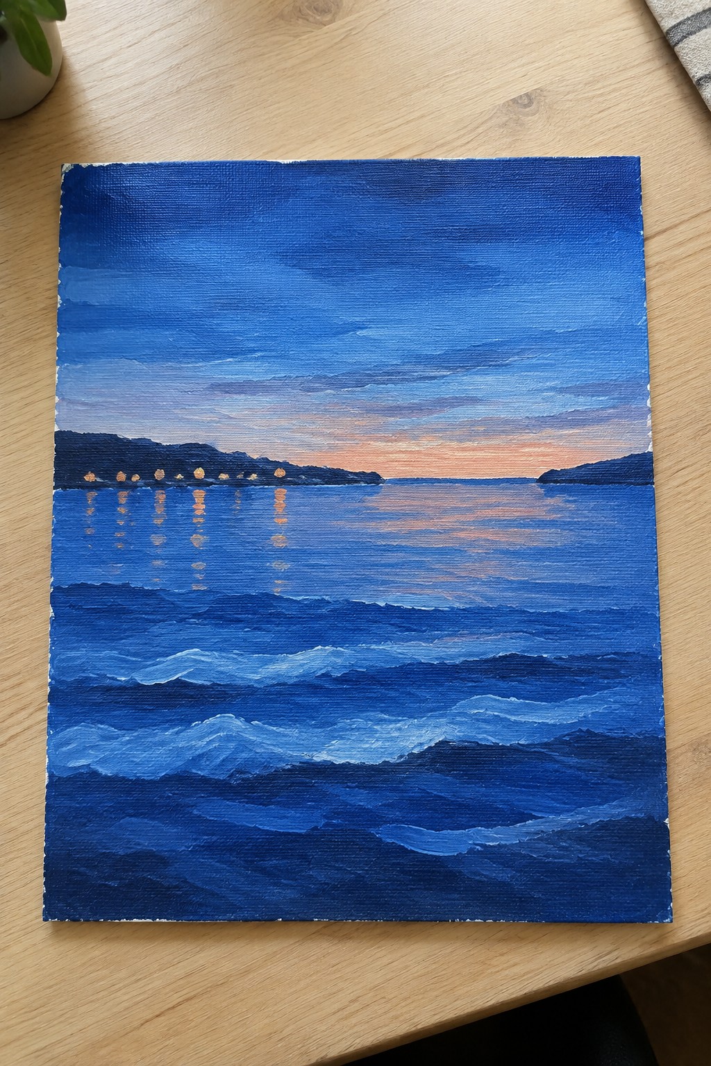 Oil painting of blue waves at sunset with glowing shoreline reflections on canvas
