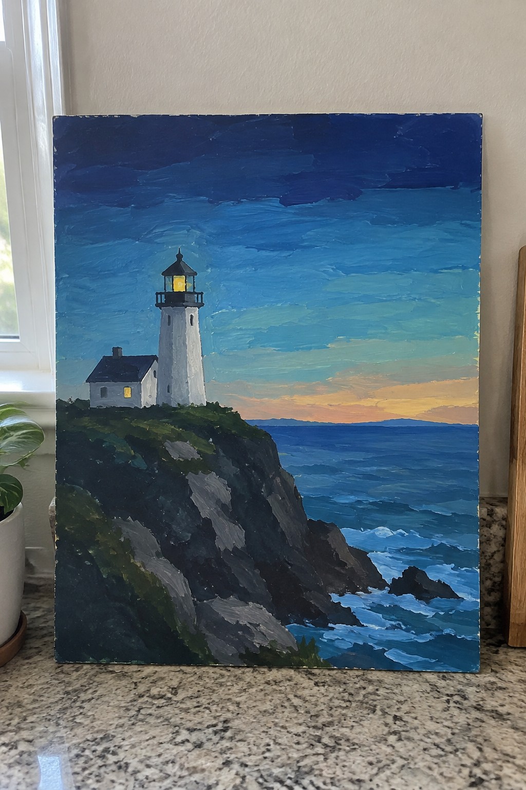 White lighthouse with glowing light atop rocky cliff by blue ocean at sunset