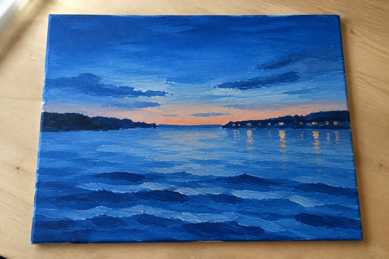 Oil painting of blue waves at sunset with glowing shoreline reflections on canvas