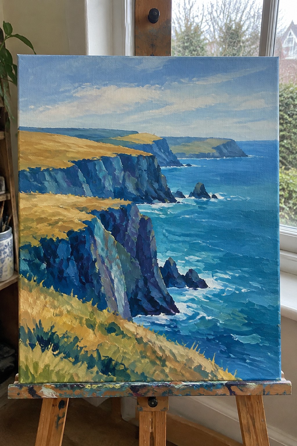 Vivid painting of blue cliffs and ocean waves on wooden easel in room